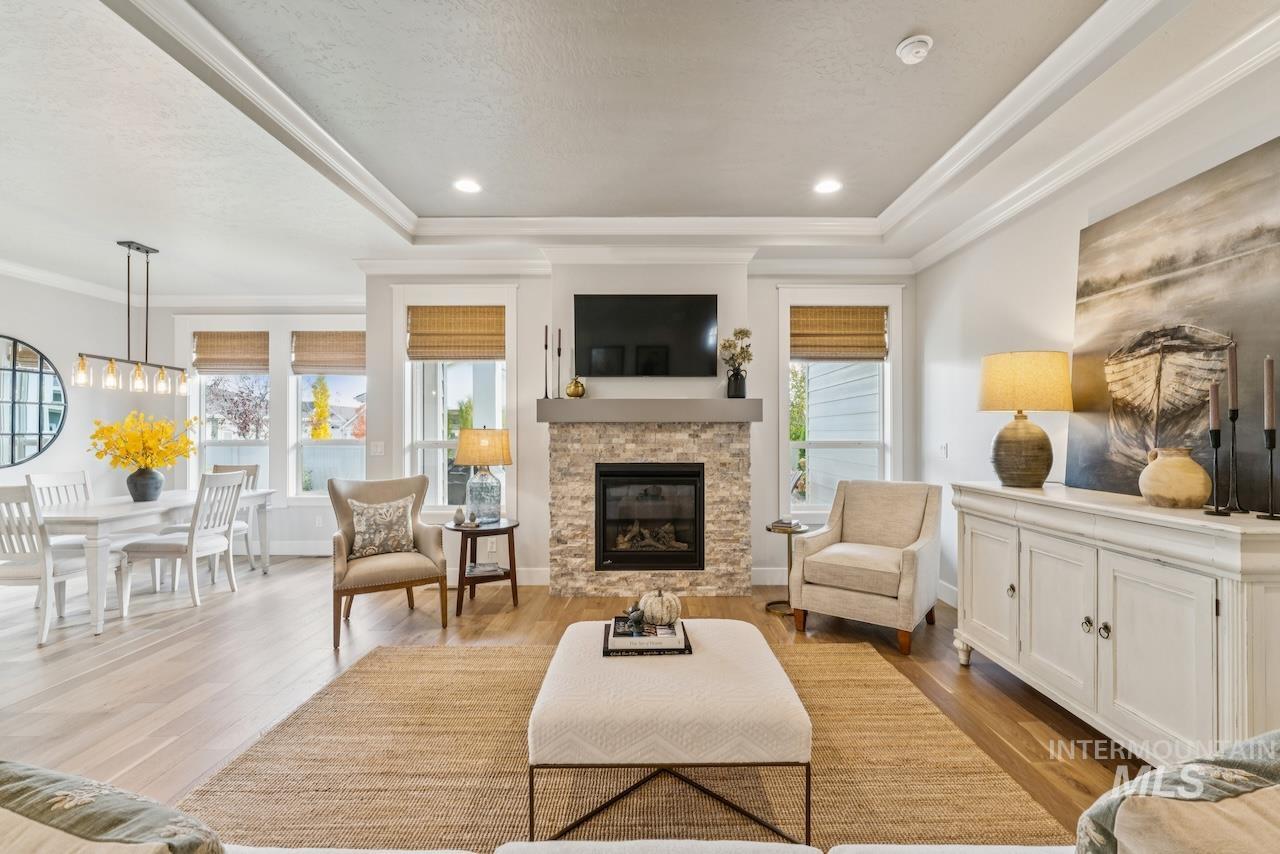 Living room featuring a raised ceiling, light wood-style flooring, a fireplace, ornamental molding, and recessed lighting