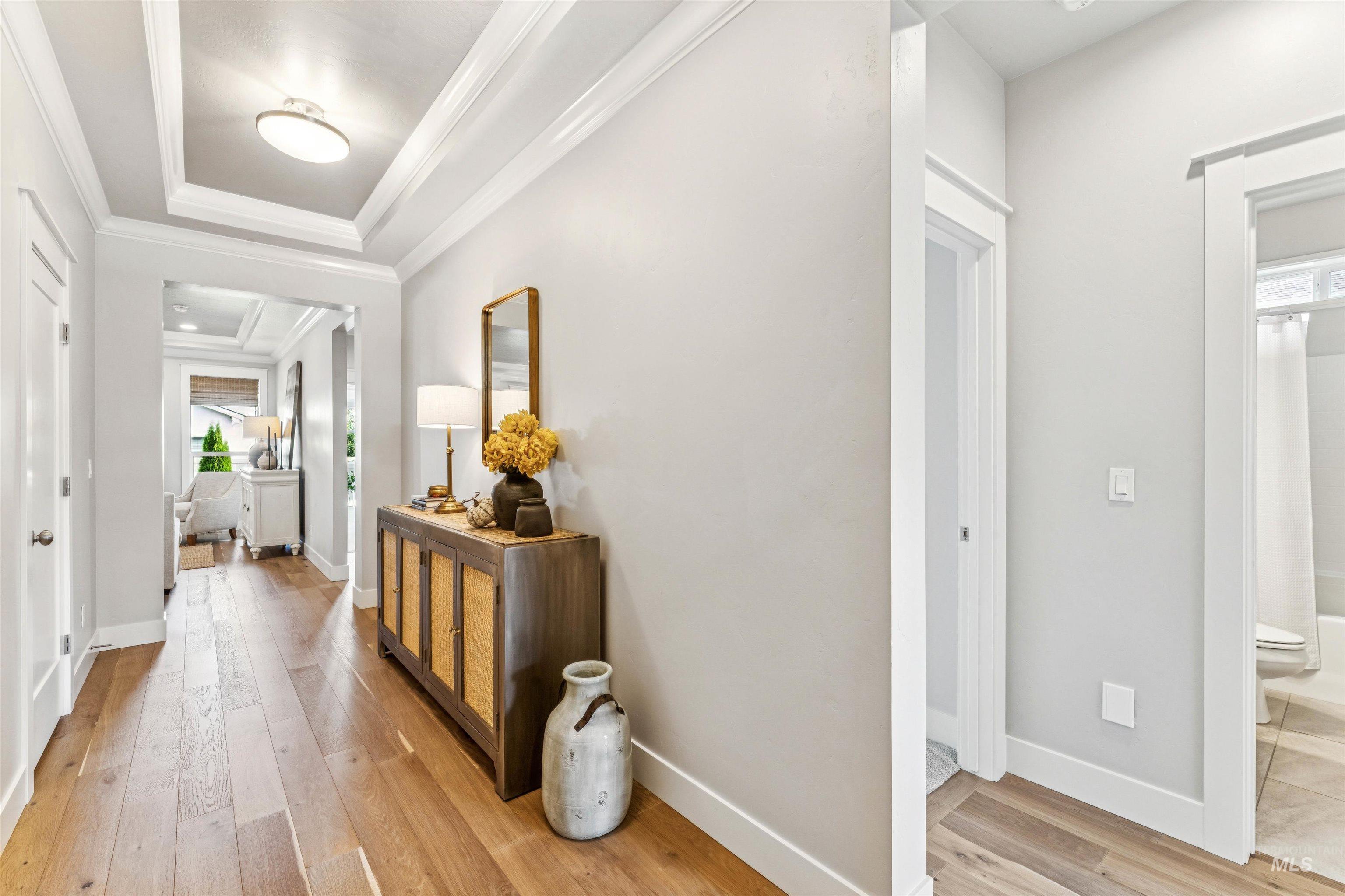 Corridor featuring light wood-style flooring, a raised ceiling, and ornamental molding