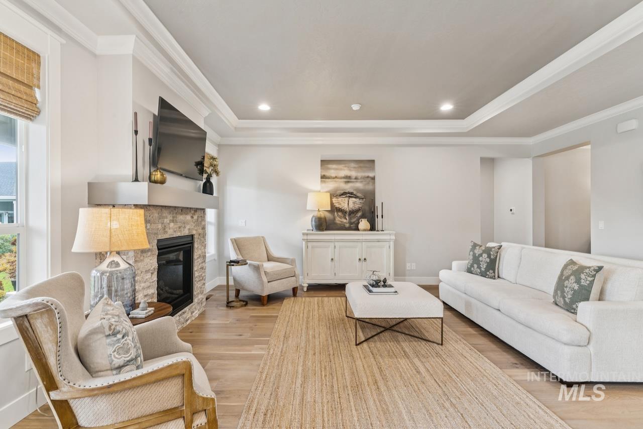Living room with light wood finished floors, a glass covered fireplace, ornamental molding, recessed lighting, and a tray ceiling