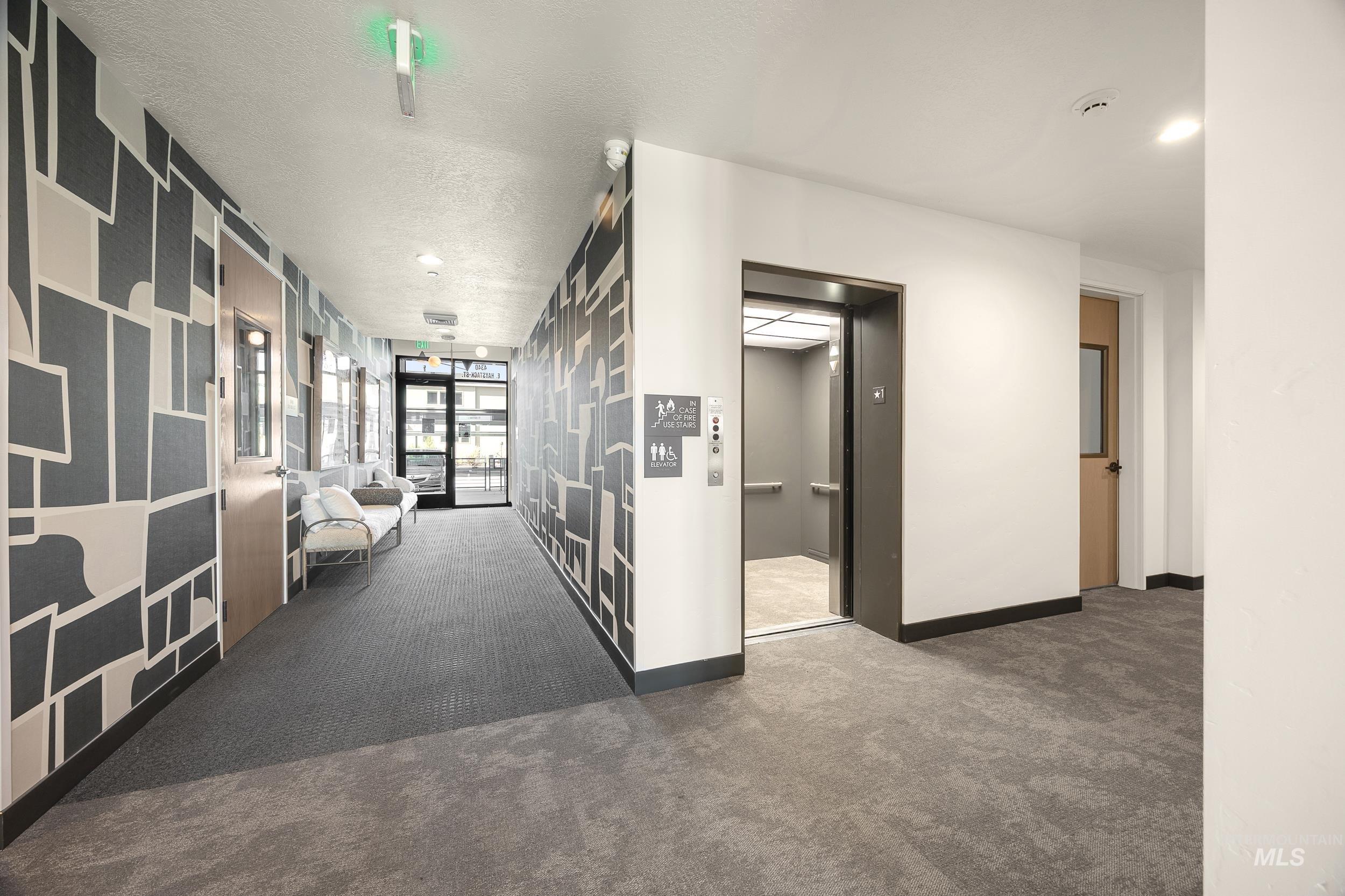 Corridor with carpet floors, elevator, a textured ceiling, and recessed lighting