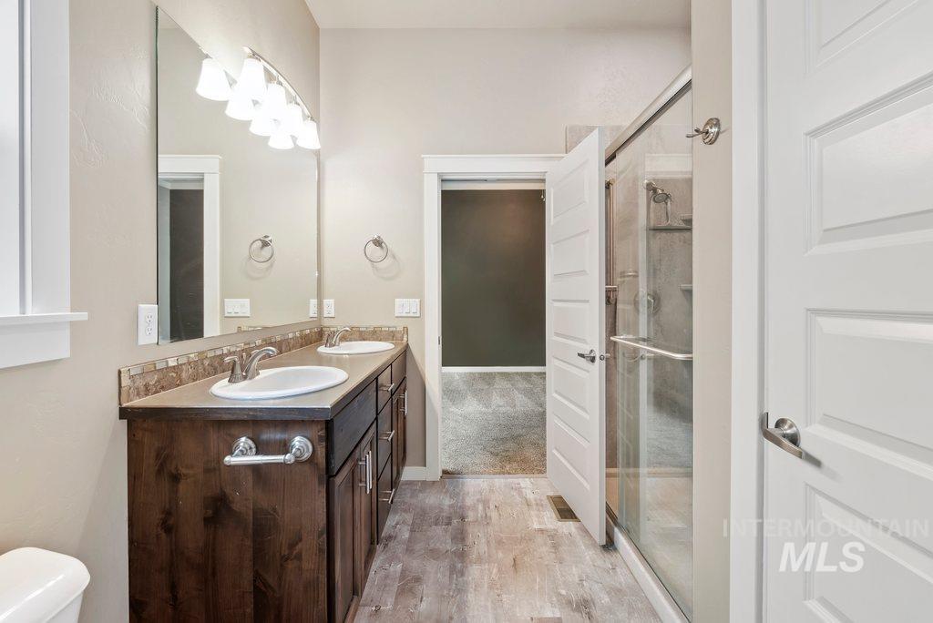 Bathroom featuring double vanity, light wood-style floors, and a stall shower