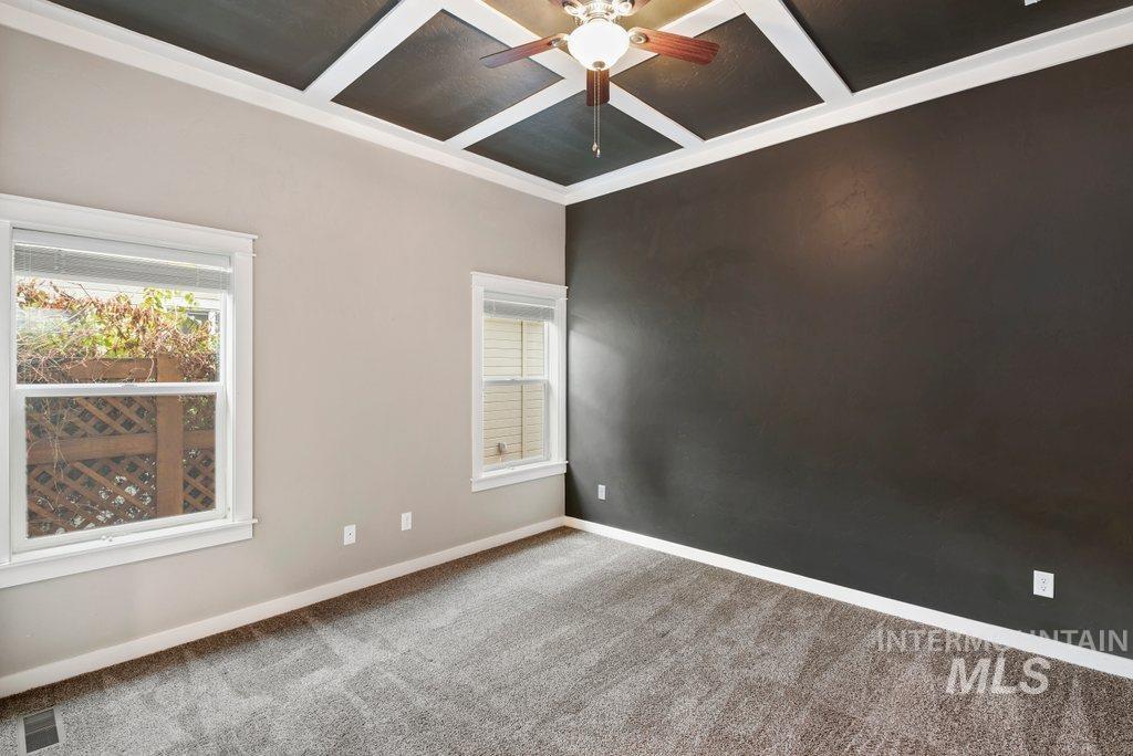 Carpeted spare room featuring coffered ceiling, healthy amount of natural light, beamed ceiling, and ceiling fan
