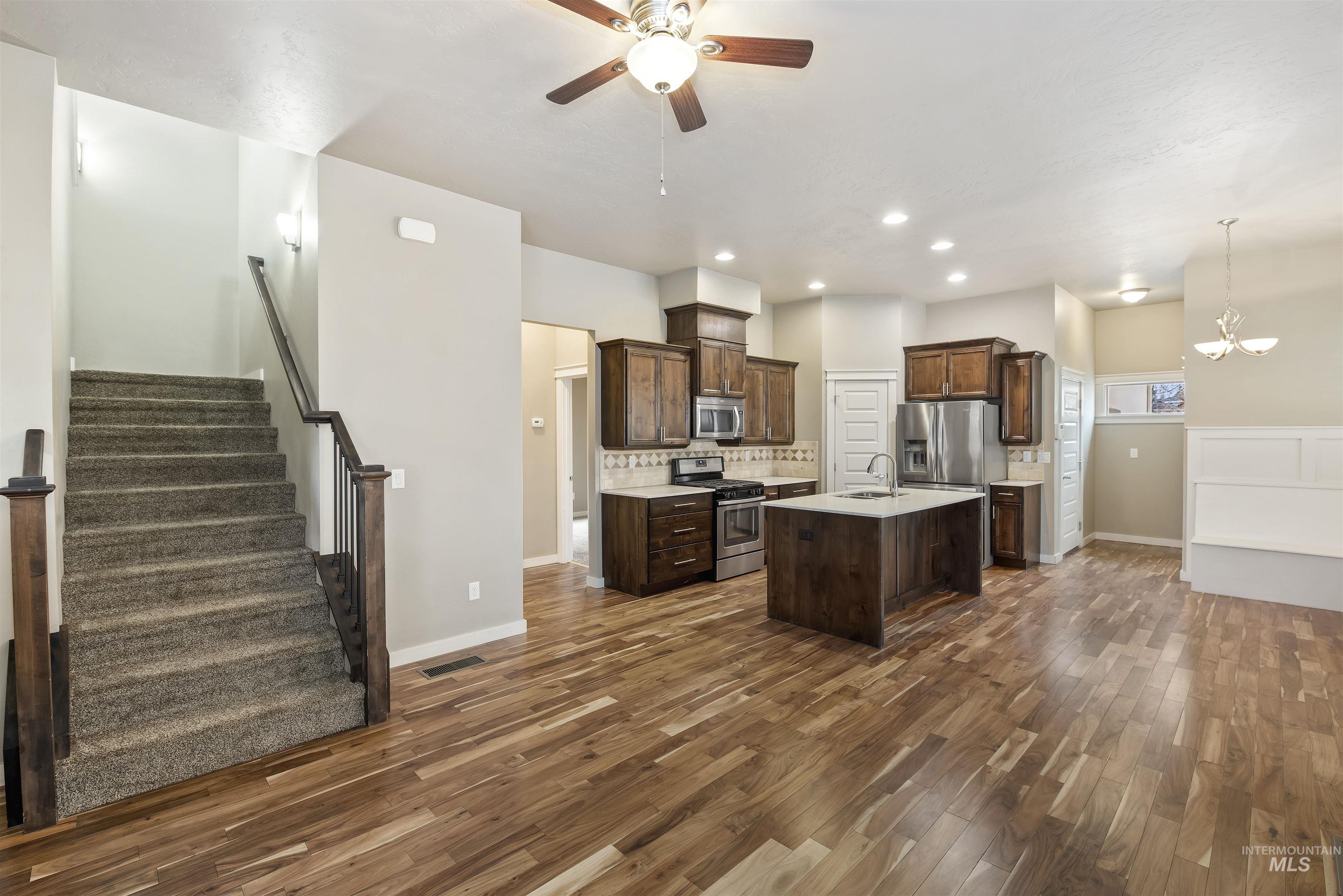 Kitchen featuring an island with sink, appliances with stainless steel finishes, tasteful backsplash, dark wood-style floors, and recessed lighting