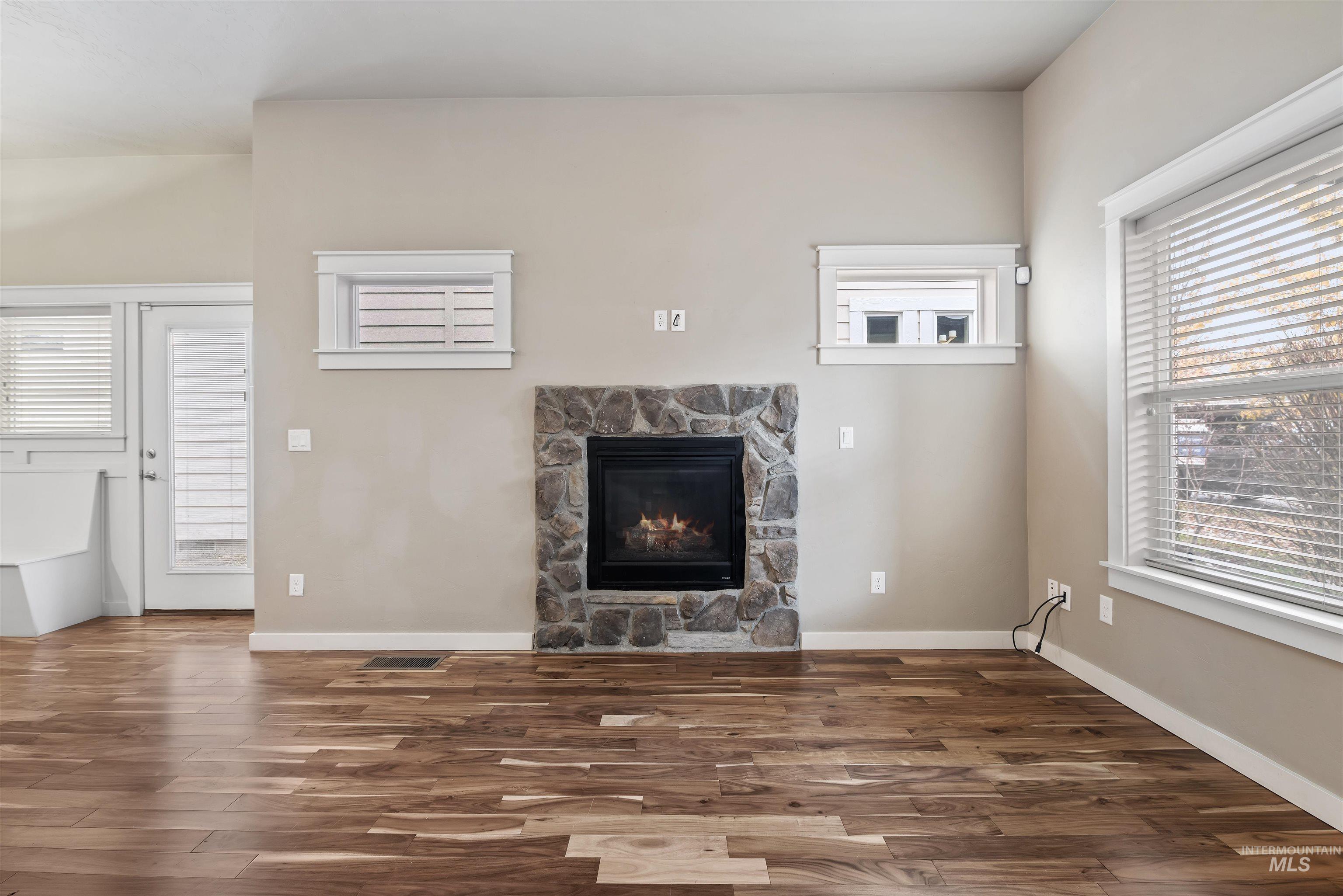 Unfurnished living room featuring a stone fireplace and dark wood-style floors