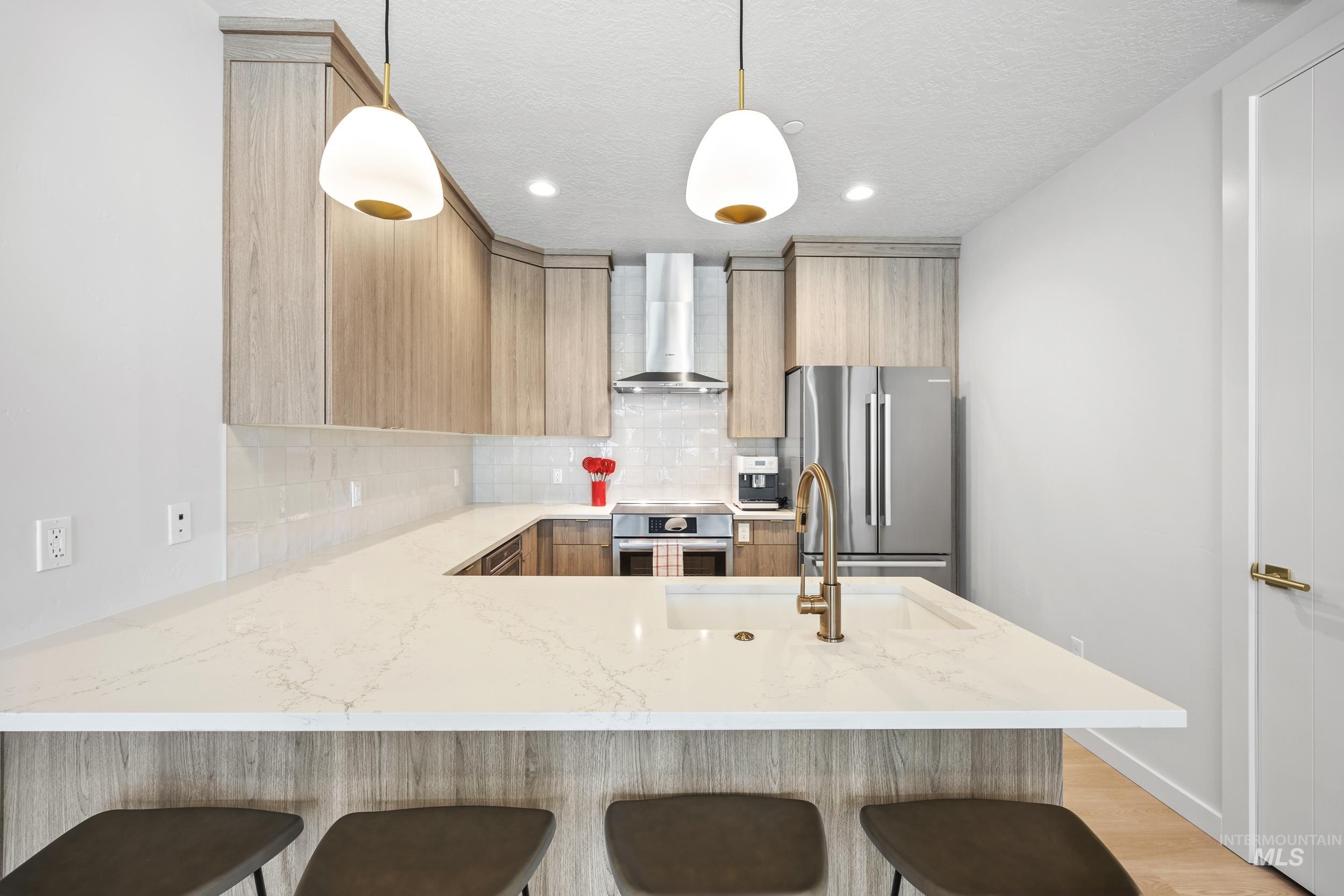 Kitchen featuring backsplash, a peninsula, stainless steel appliances, light brown cabinetry, and recessed lighting