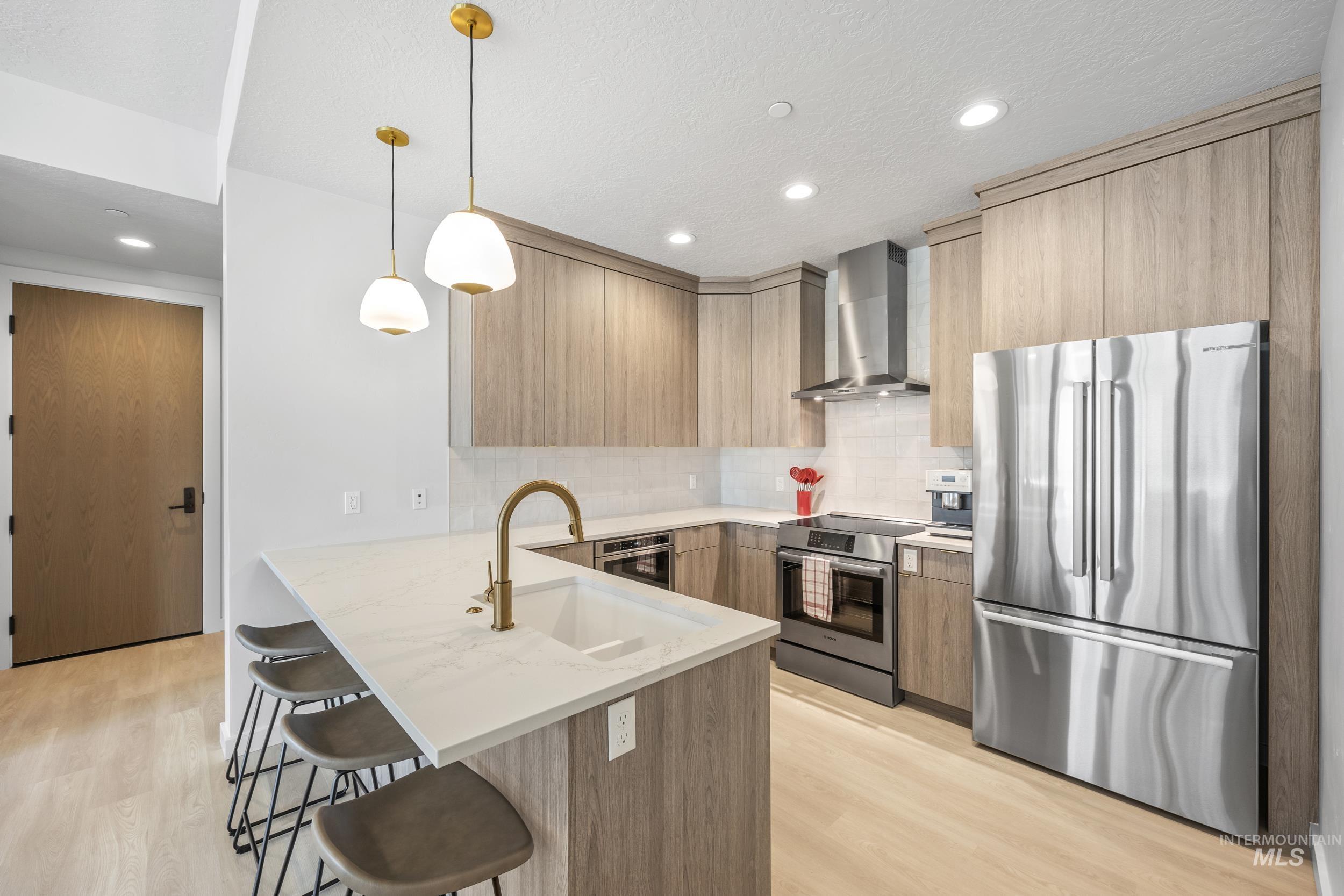 Kitchen with appliances with stainless steel finishes, a peninsula, modern cabinets, a kitchen bar, and wall chimney range hood