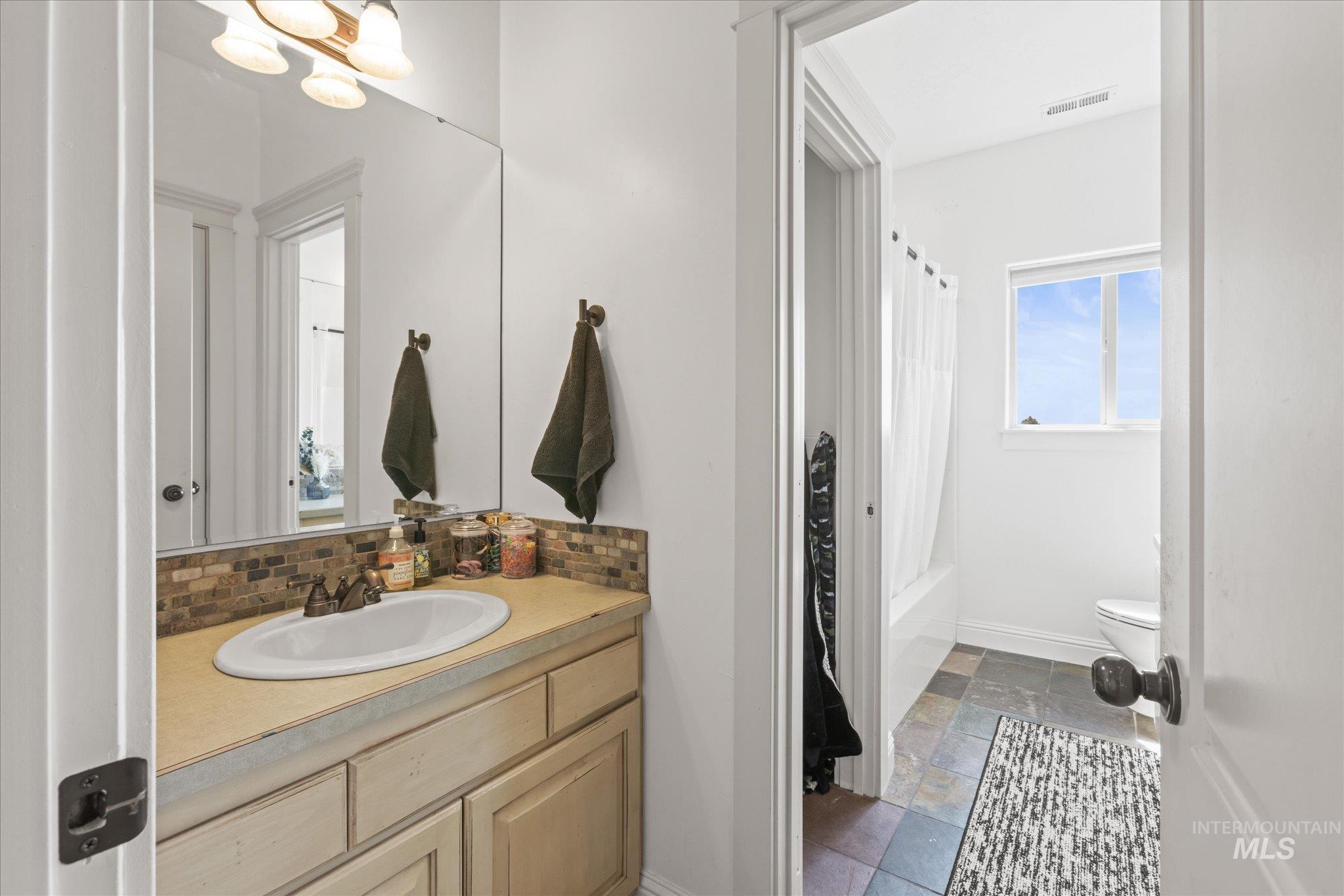 Bathroom featuring a vanity with an oval undermount sink, a backsplash with mosaic tile, and a wall-mounted mirror