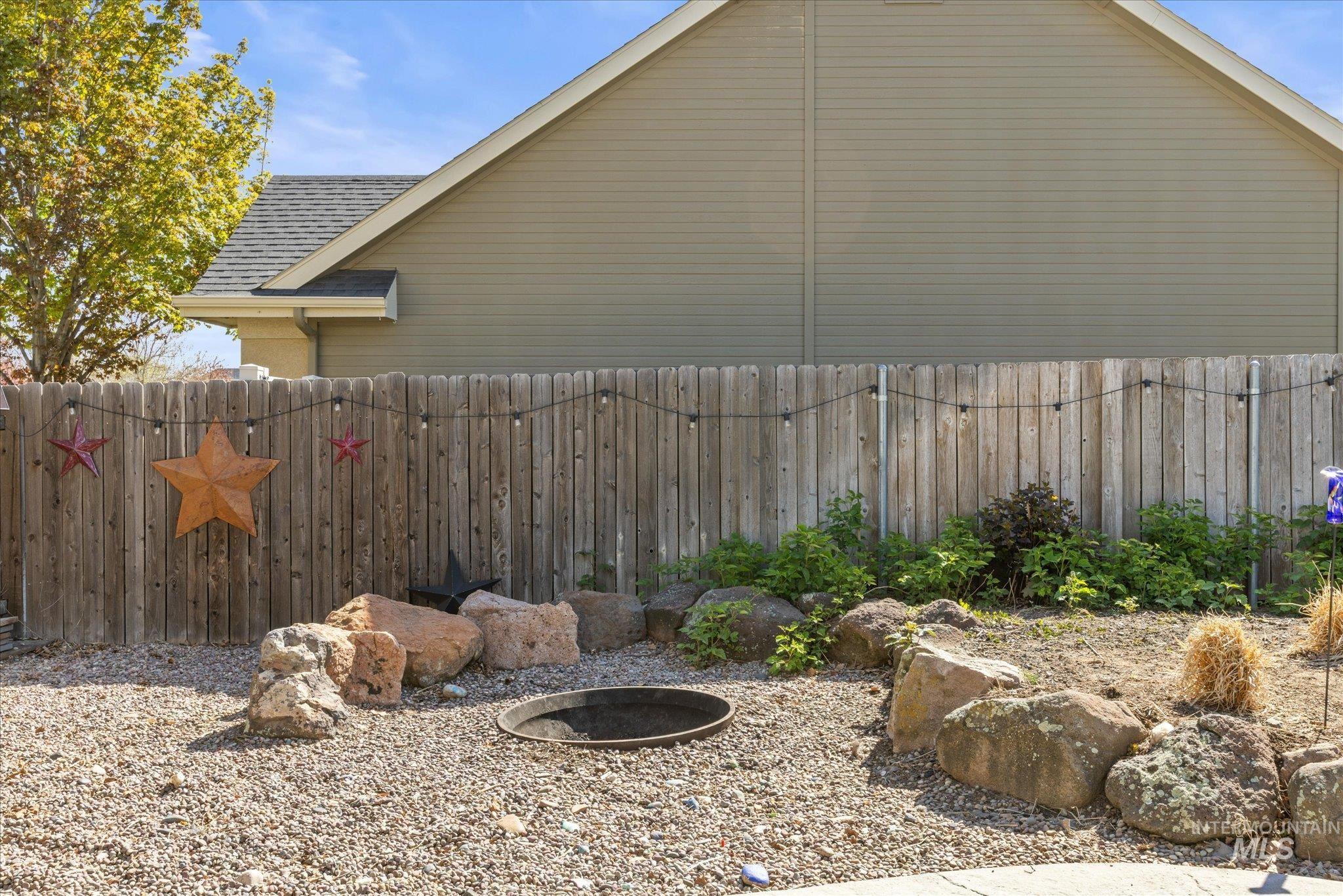Gravel patio area featuring a built-in fire pit, surrounded by natural rock landscaping and a privacy fence