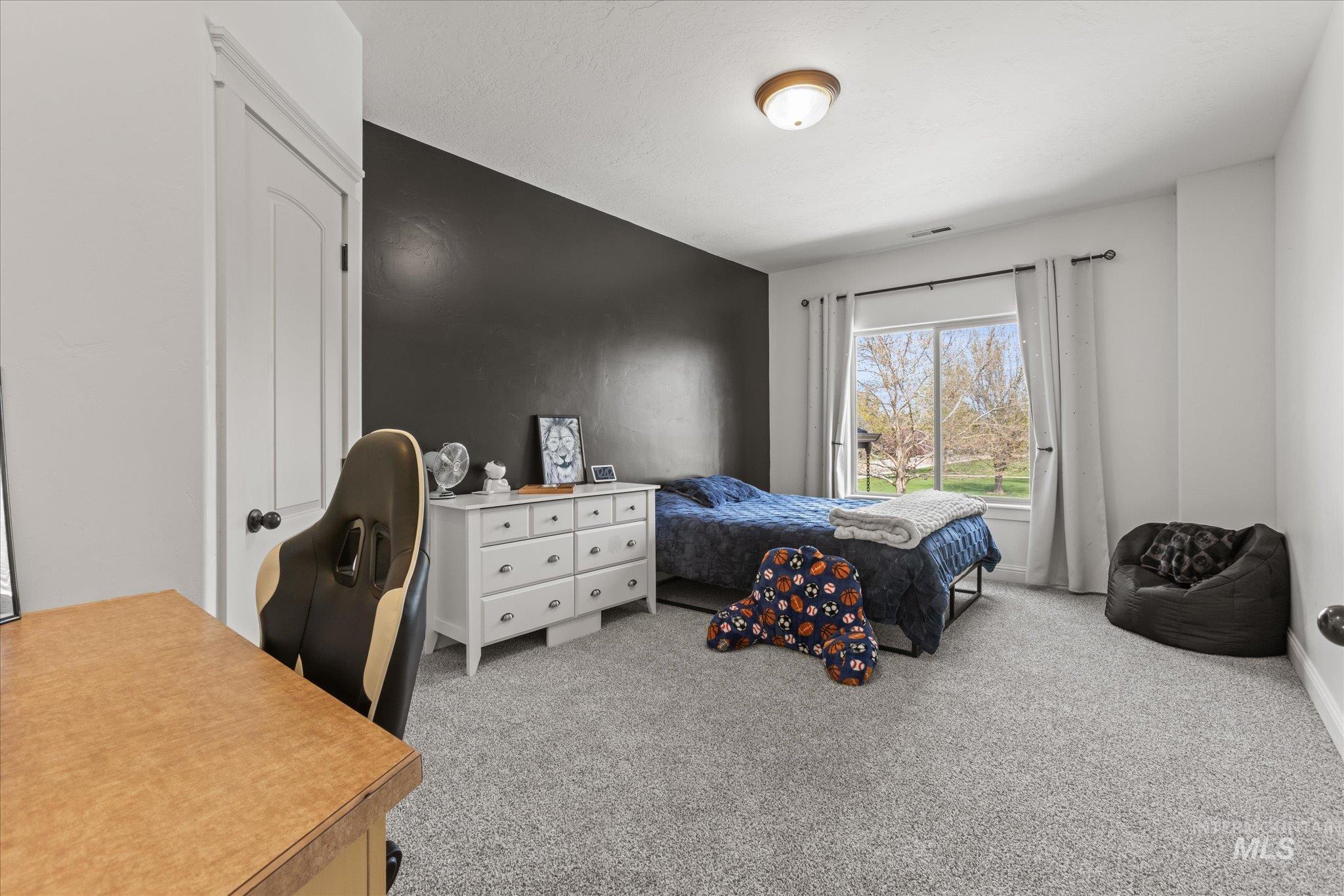 Carpeted room with a prominent window, white trim, and a dark accent wall