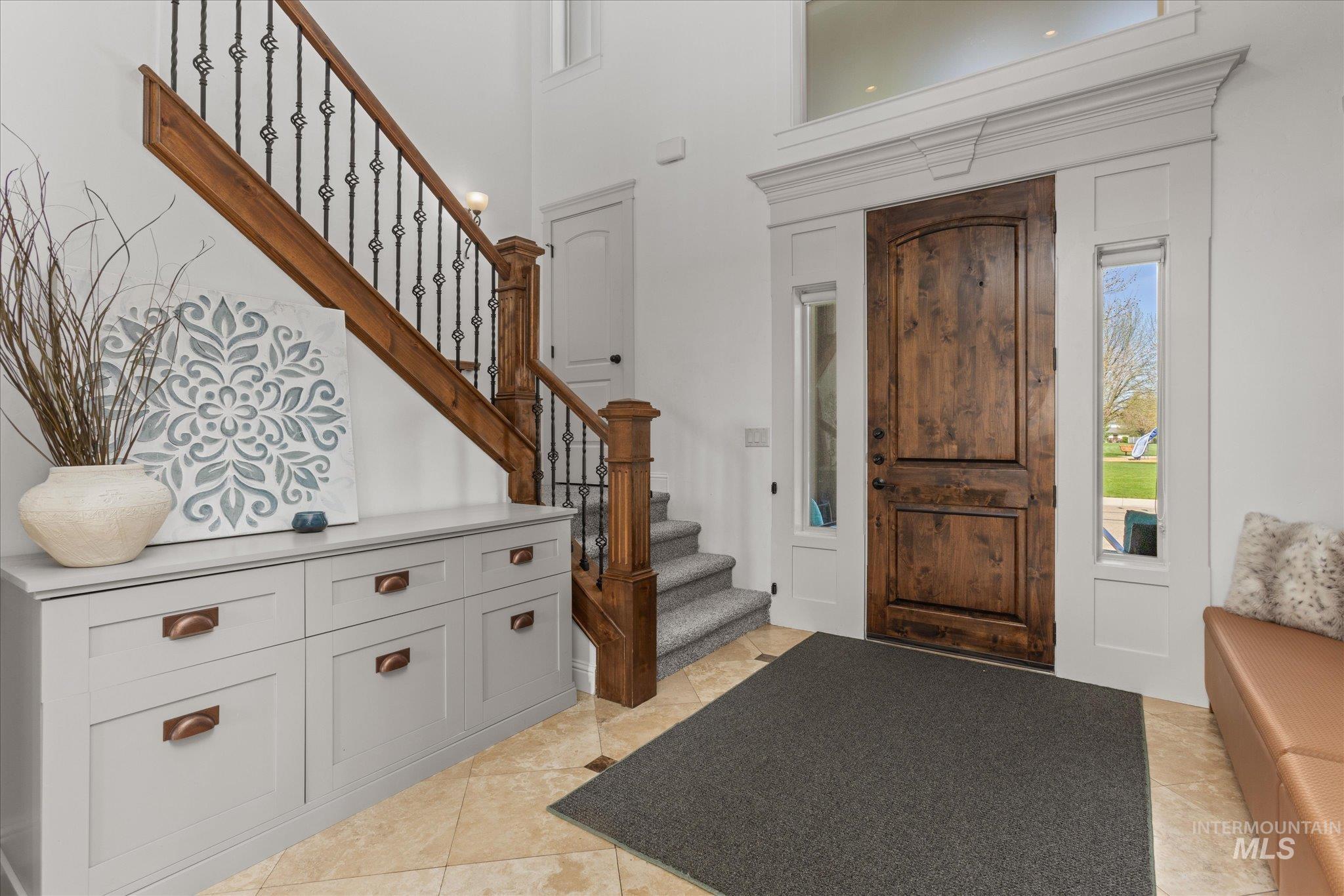 Grand entryway featuring a custom wood door with sidelights and transom window, an ornate wrought iron and wood staircase, and tiled flooring