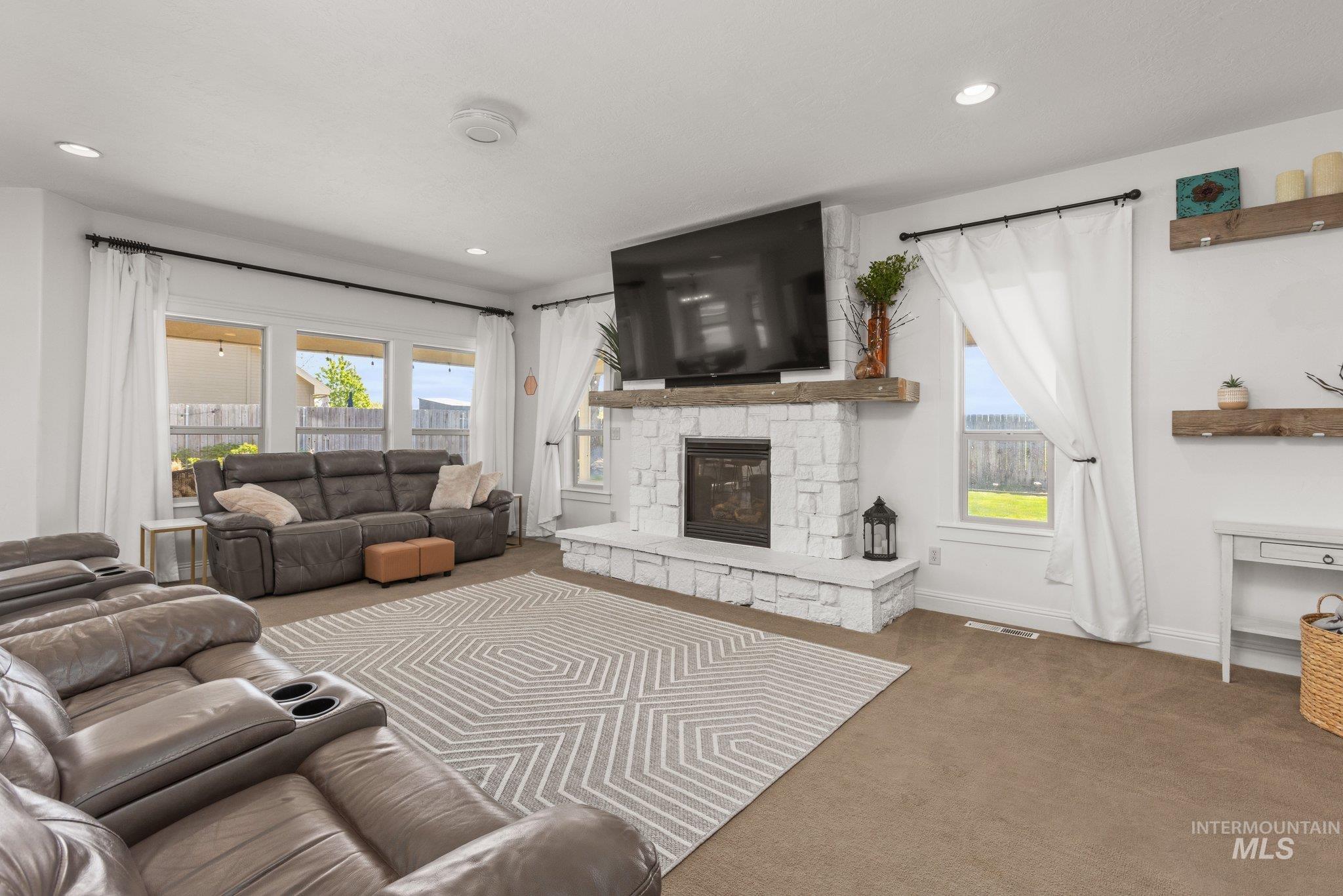 Living area featuring a stone-clad fireplace with a wood mantel, recessed lighting, and a series of windows