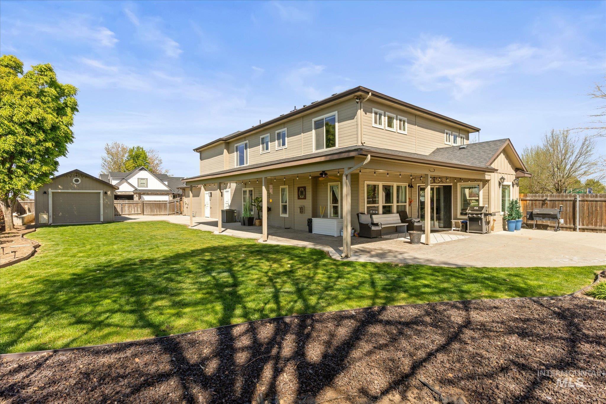 Expansive backyard featuring a manicured lawn, a detached single-car garage, and a covered patio with string lighting