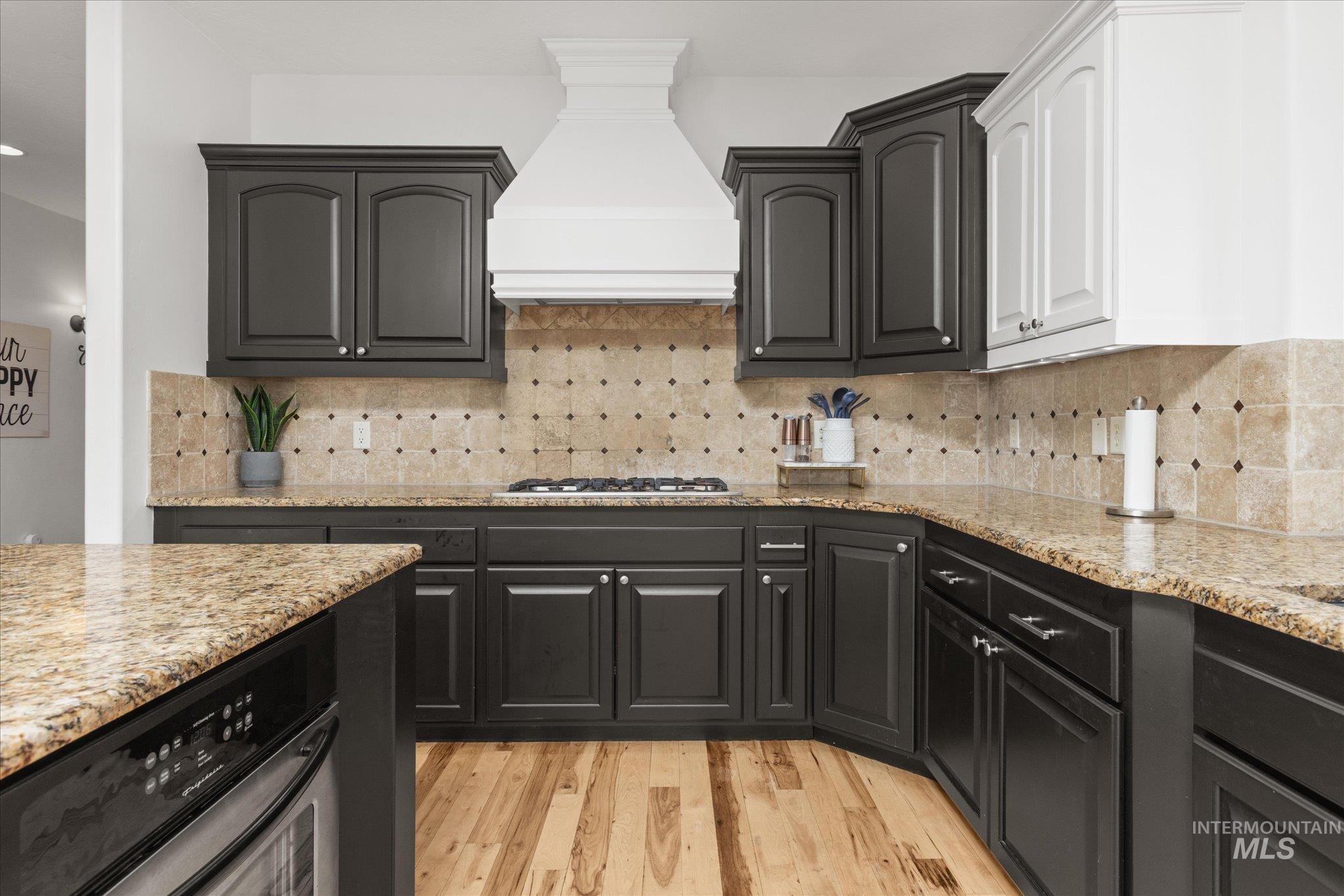 Kitchen featuring wood-finish flooring, two-tone cabinetry with black lower and white upper cabinets, granite countertops, and a tiled backsplash