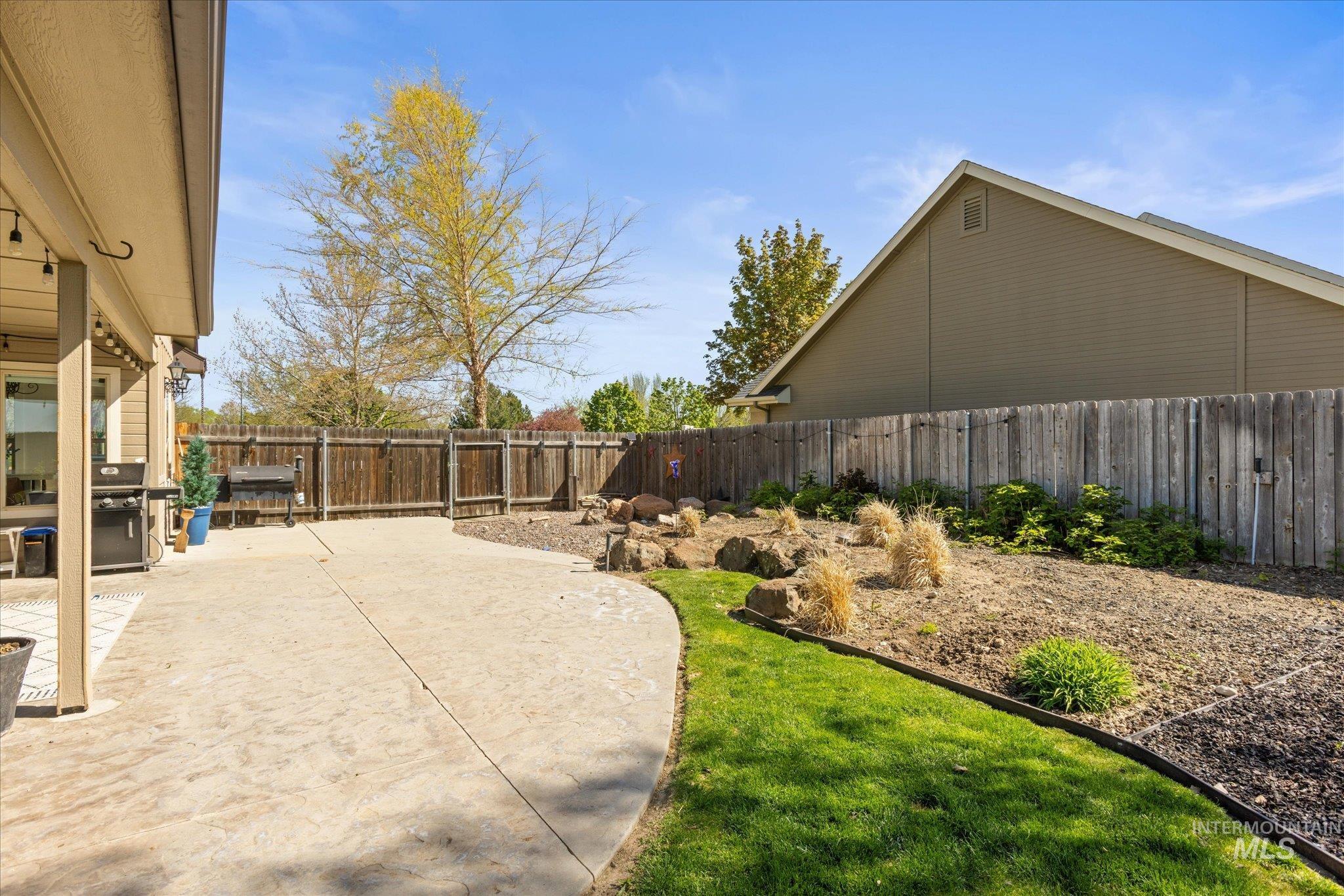 Expansive concrete patio area with a covered extension, complemented by a sloped rock garden and a partial lawn