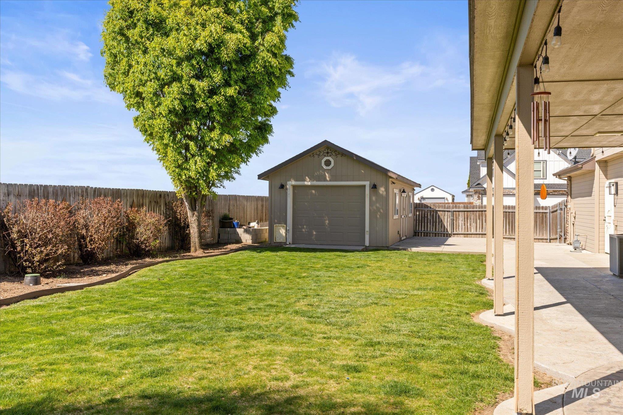 Expansive backyard featuring a manicured lawn, a detached garage, and a covered patio with concrete flooring