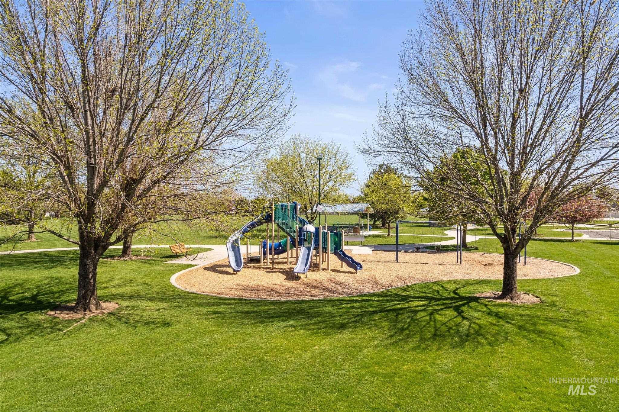 Park setting featuring a playground with slides and climbing structures on a wood chip base