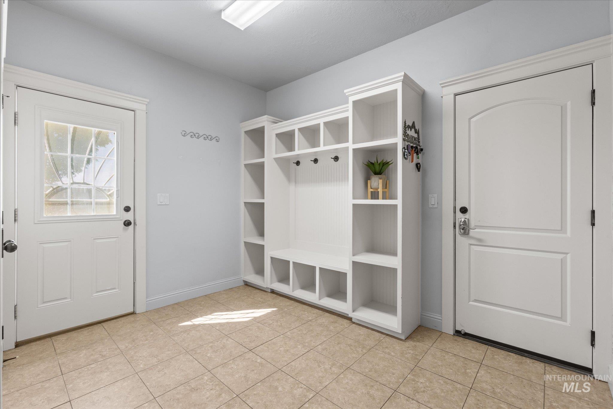 Entryway featuring a built-in white storage unit with cubbies and hooks, tiled flooring, a door with decorative glass inserts, and a second solid panel door