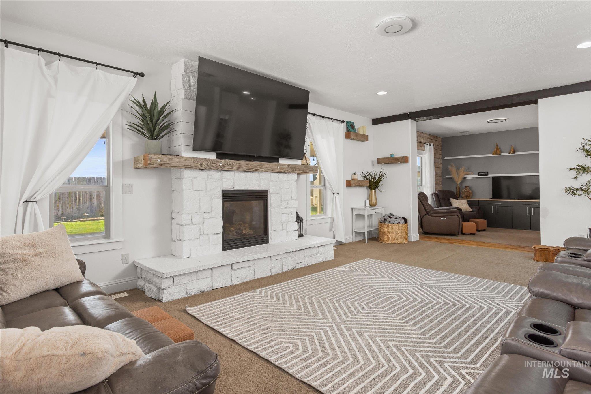 Spacious living area featuring a white stone-clad fireplace with a rustic wood mantel