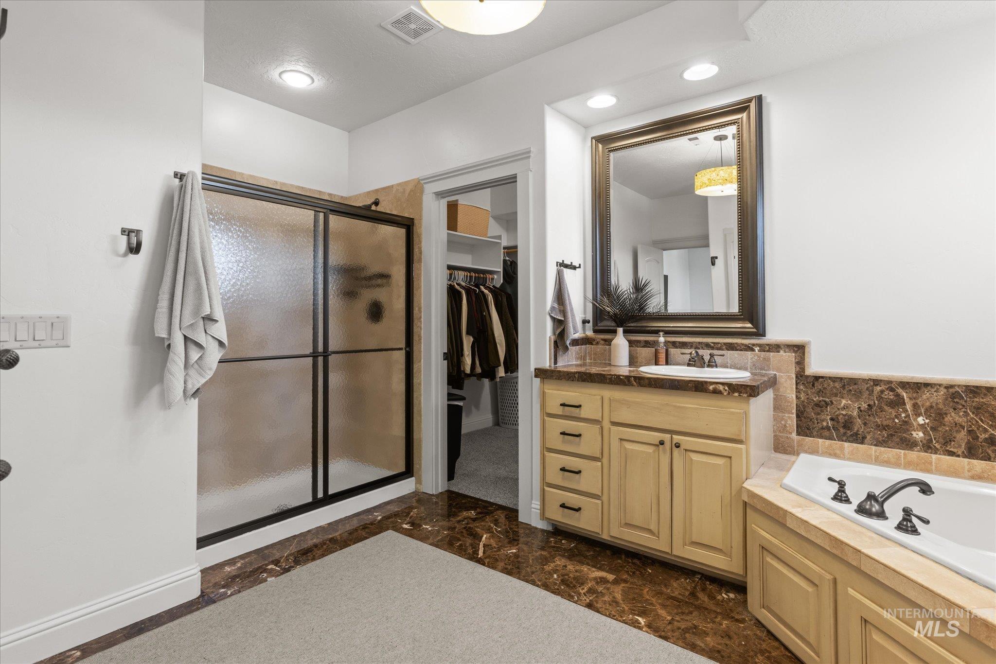 Bathroom featuring a sliding glass shower enclosure, a vanity with an integrated sink and base cabinetry, a framed mirror, a built-in corner bathtub, and polished stone flooring