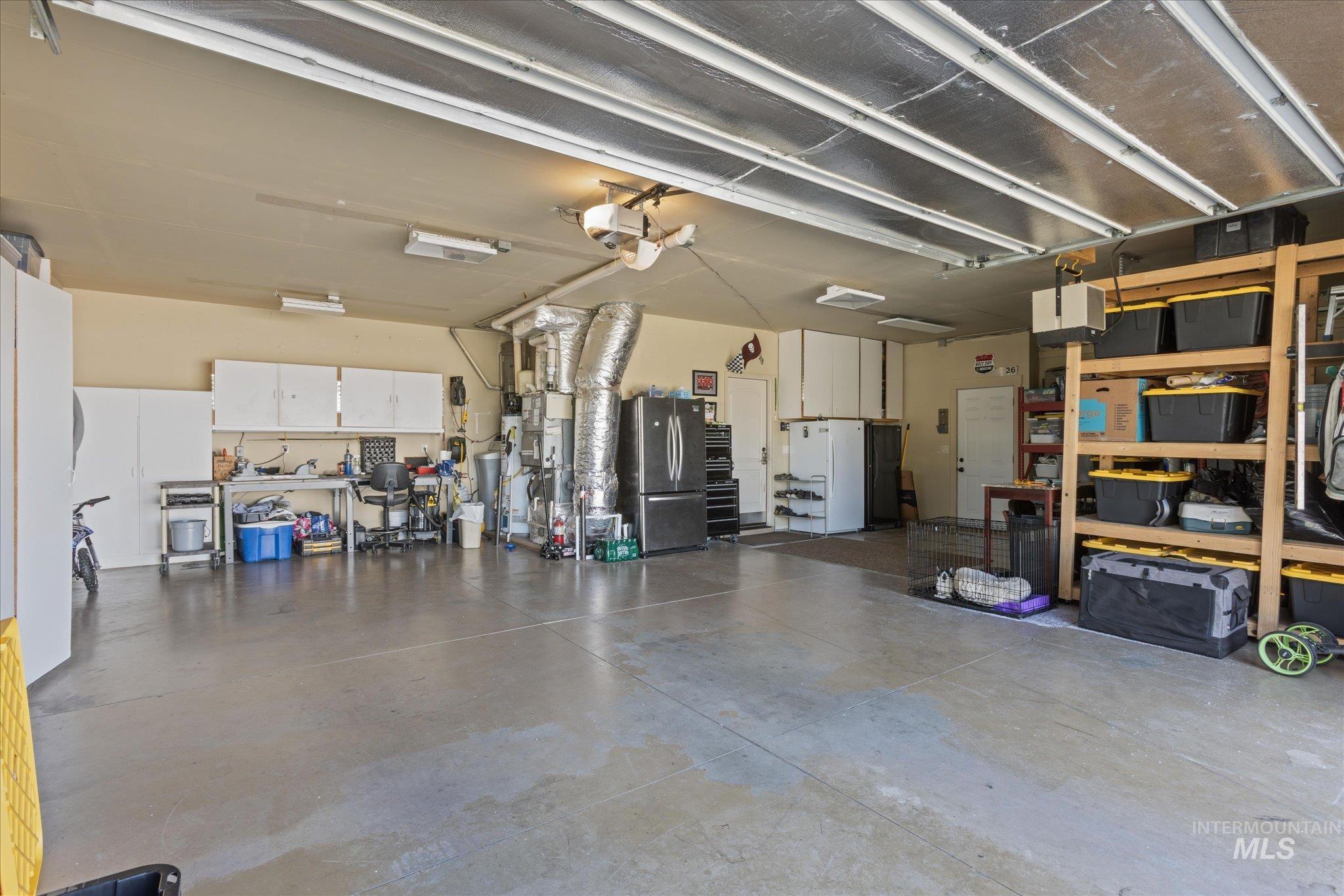 Spacious garage featuring a concrete floor, overhead fluorescent lighting, built-in white cabinetry, a dedicated workbench area, and extensive shelving units