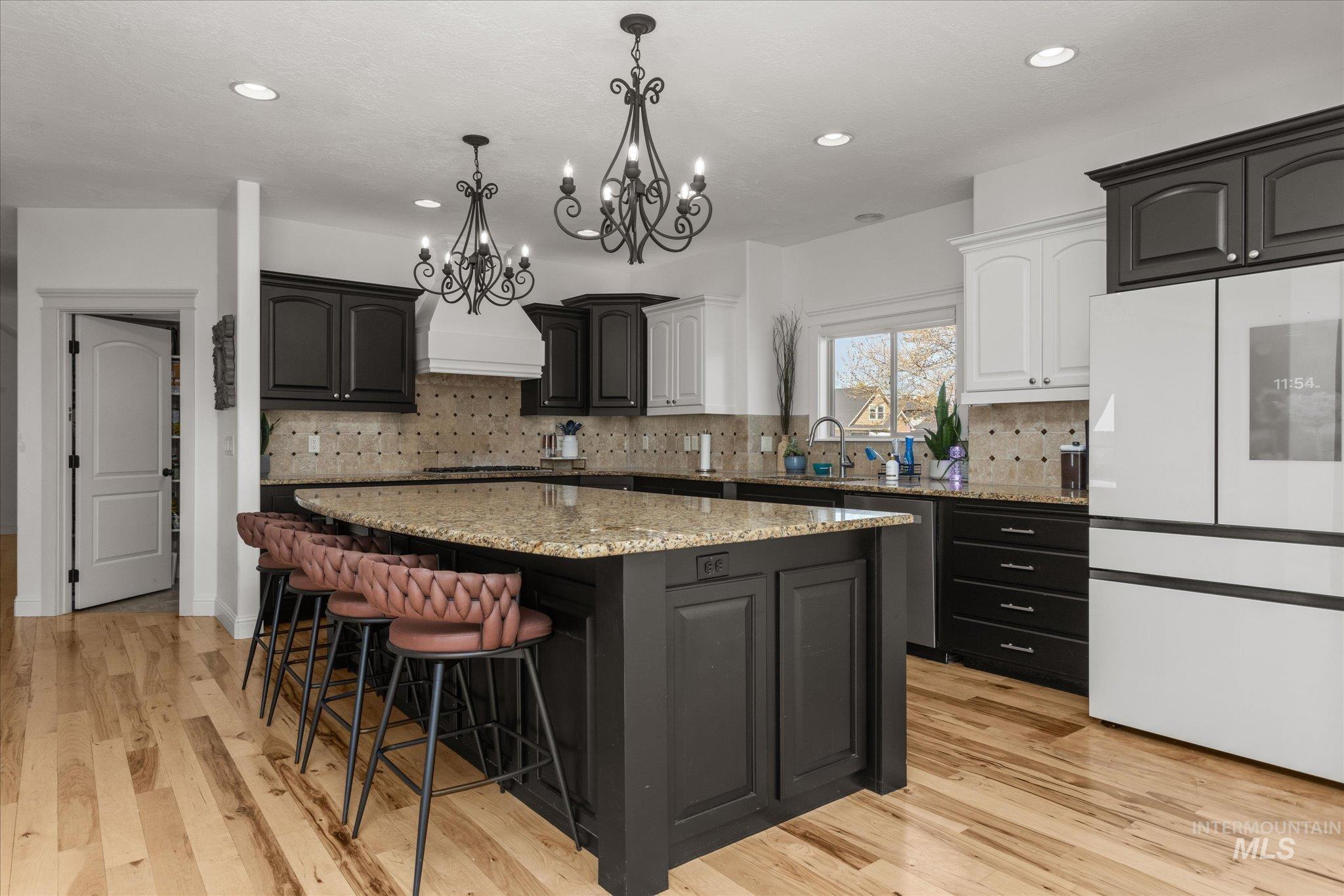 Spacious kitchen featuring a large island with a stone-finish countertop, dual-tone cabinetry, and wood-finish flooring