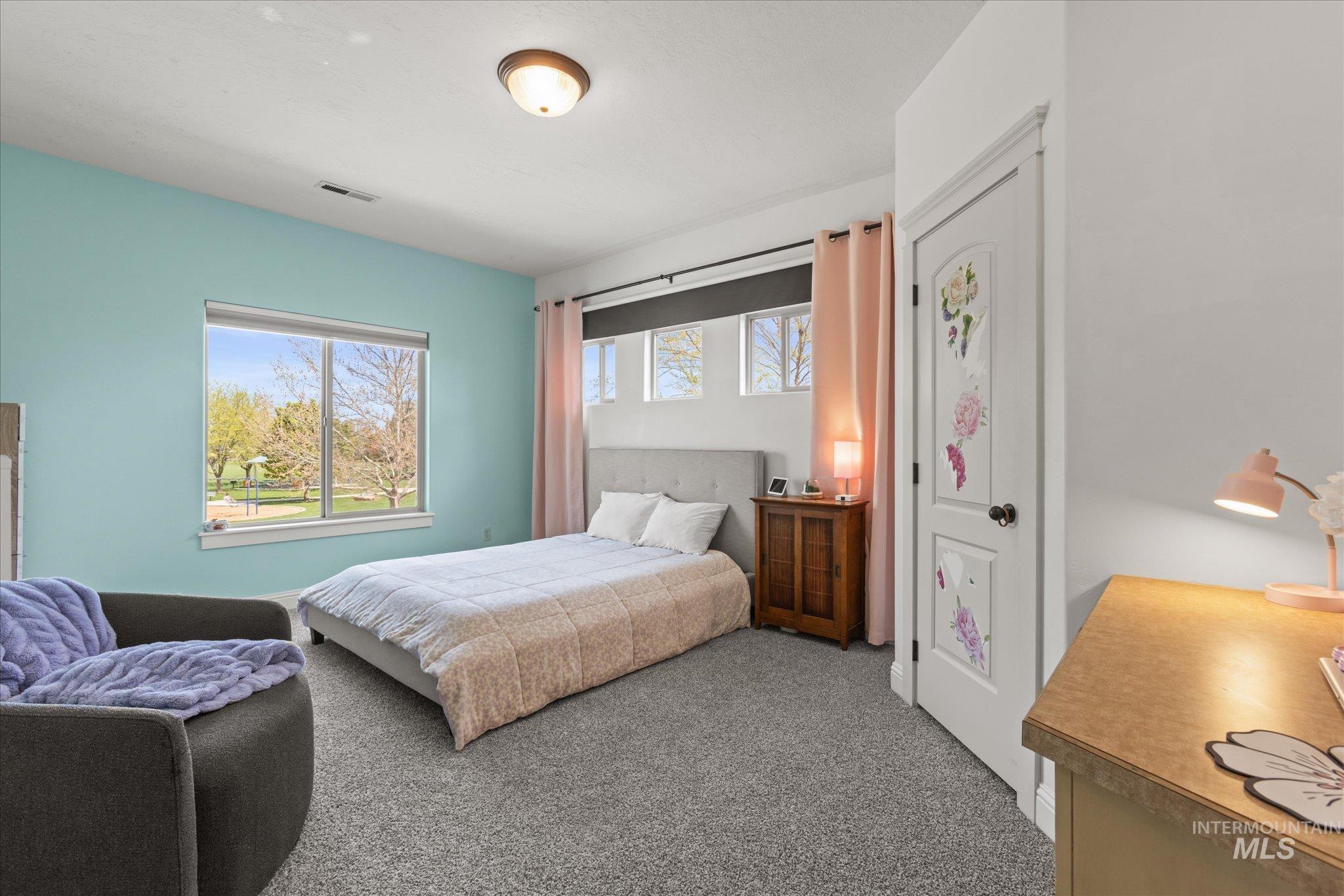 Spacious room featuring a large window, light blue accent wall, white trim, and gray carpet