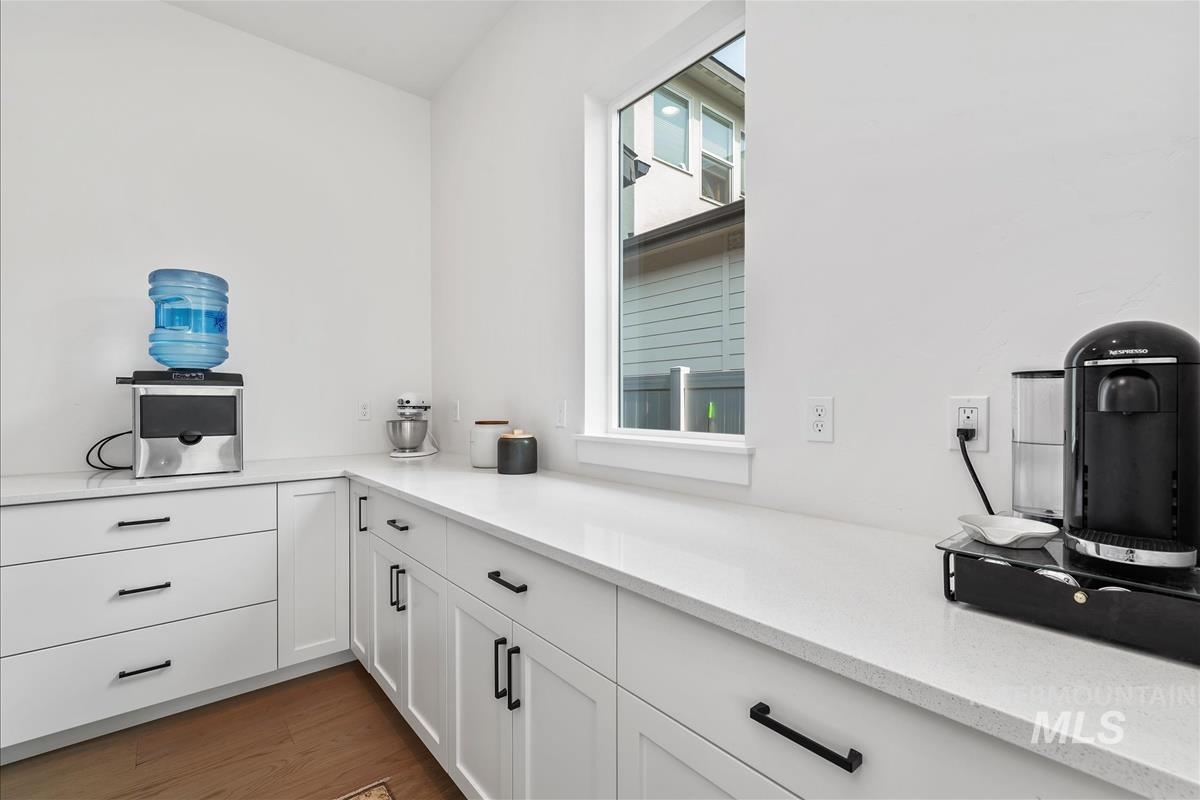 Bar area with white cabinets, dark wood-style flooring, and light stone countertops