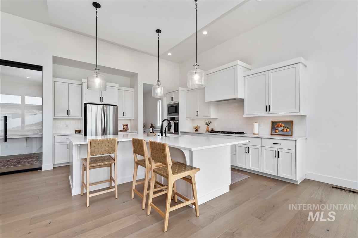 Kitchen featuring a breakfast bar, pendant lighting, backsplash, light wood finished floors, and white cabinetry