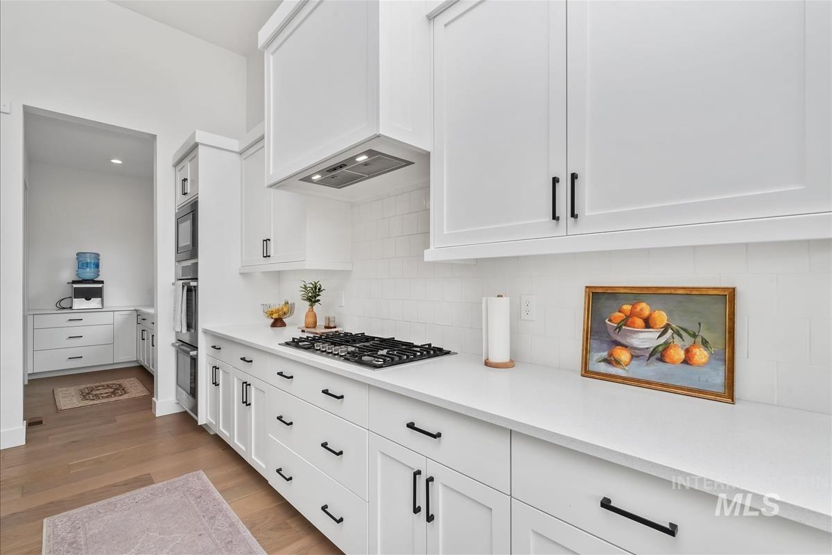 Kitchen with white cabinetry, light wood-style flooring, decorative backsplash, stainless steel appliances, and recessed lighting
