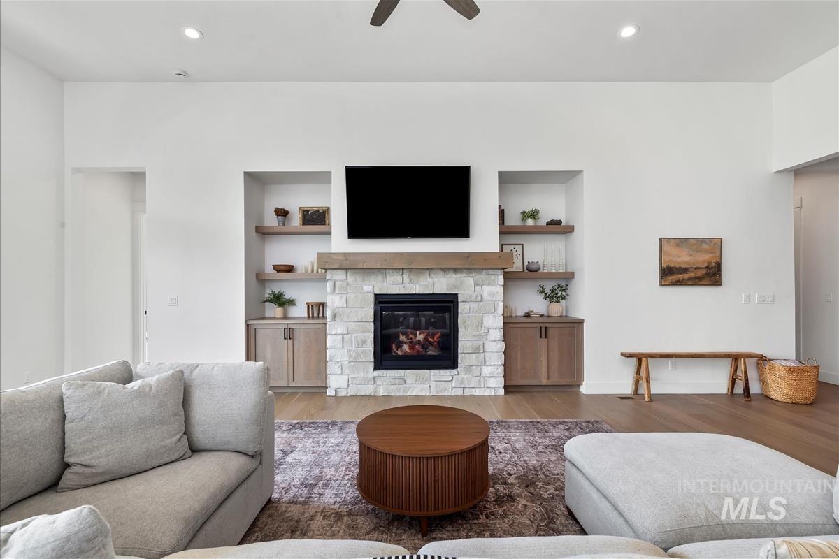 Living room featuring recessed lighting, wood finished floors, a stone fireplace, ceiling fan, and built in features