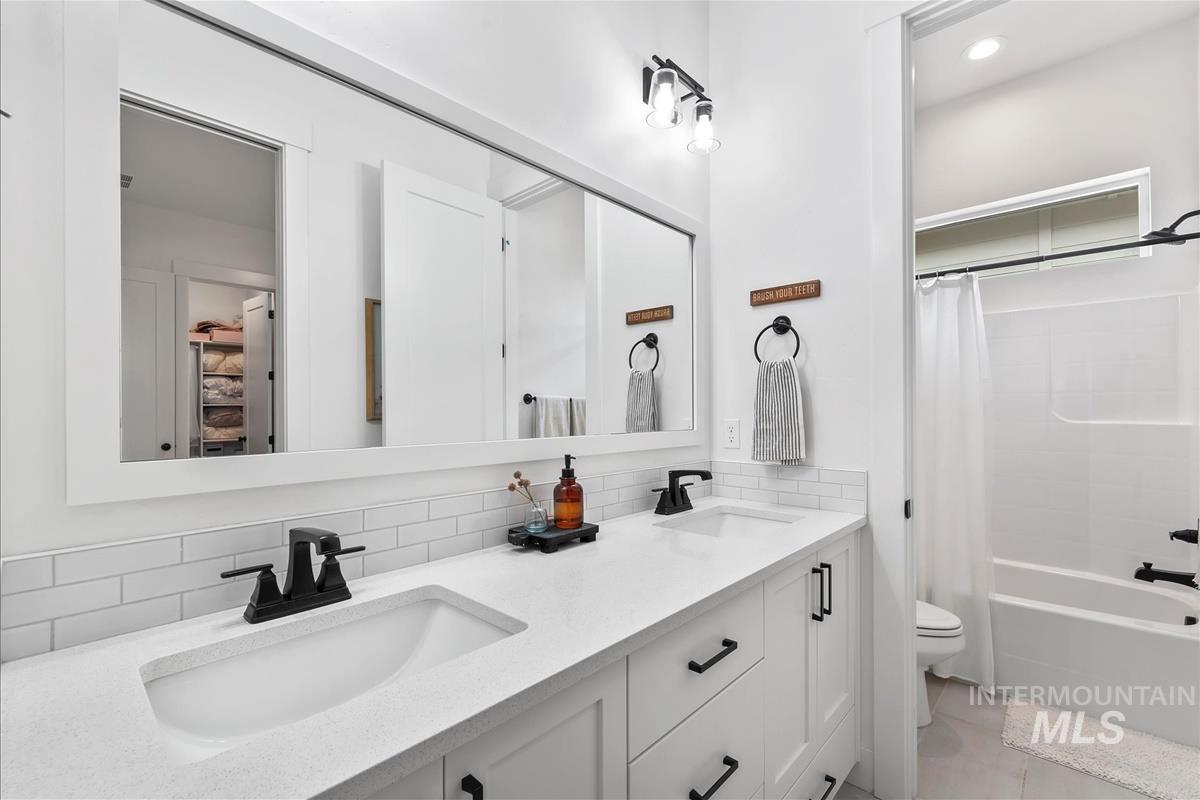 Full bath featuring decorative backsplash, shower / tub combo with curtain, double vanity, and light tile patterned floors