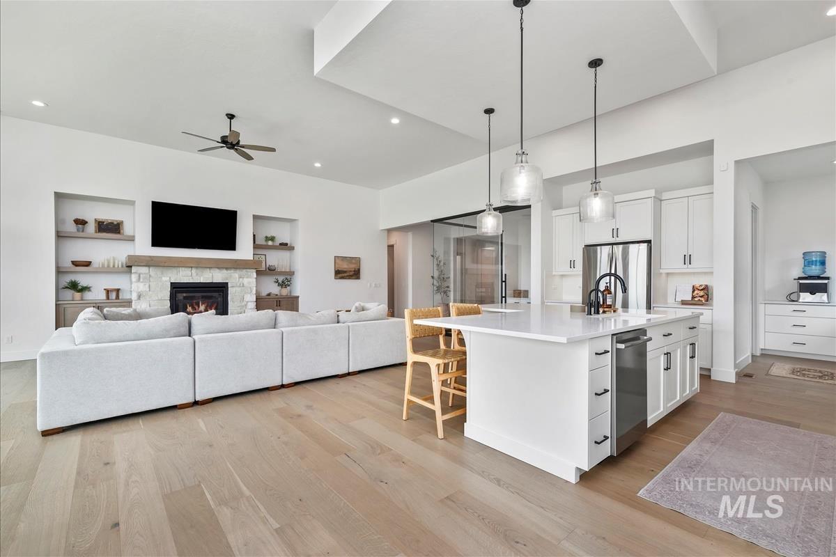 Kitchen featuring light wood-style floors, white cabinetry, a kitchen island with sink, pendant lighting, and open floor plan