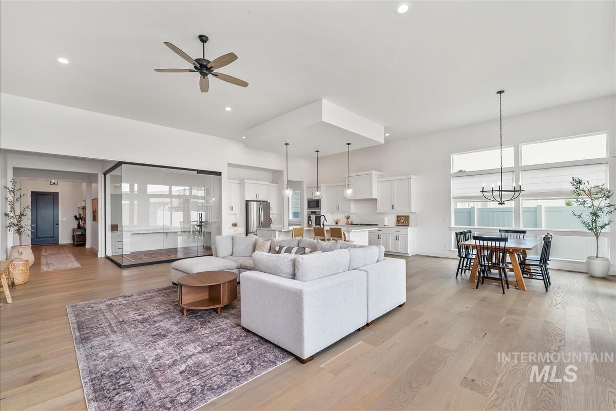 Living room with light wood-style flooring, plenty of natural light, a ceiling fan, recessed lighting, and a chandelier