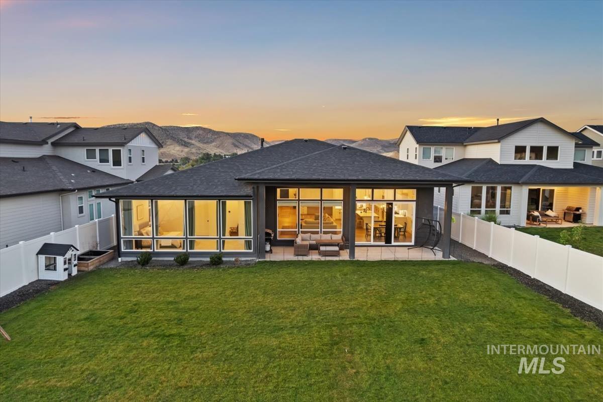 Back of house at dusk with a patio area, a fenced backyard, roof with shingles, a mountain view, and an outdoor hangout area