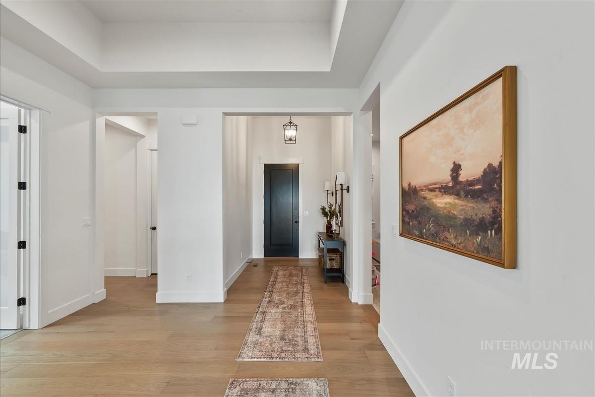 Corridor with light wood-style floors and a tray ceiling
