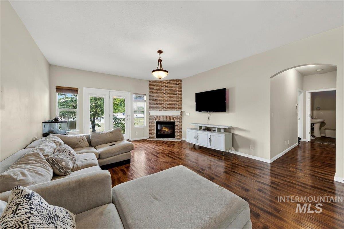 Corner brick fireplace with a white mantel, wood-finish flooring, vaulted ceiling, arched doorway, and French doors to the exterior