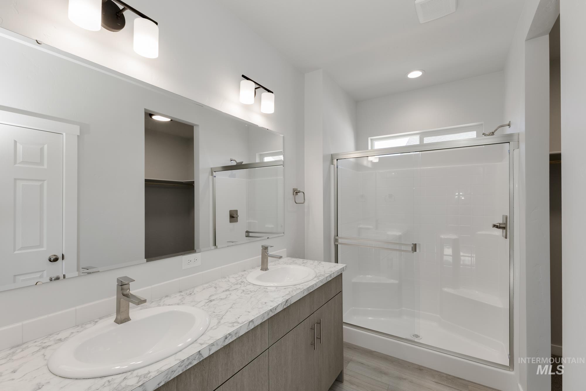 Bathroom with a stall shower, double vanity, light wood finished floors, recessed lighting, and a spacious closet