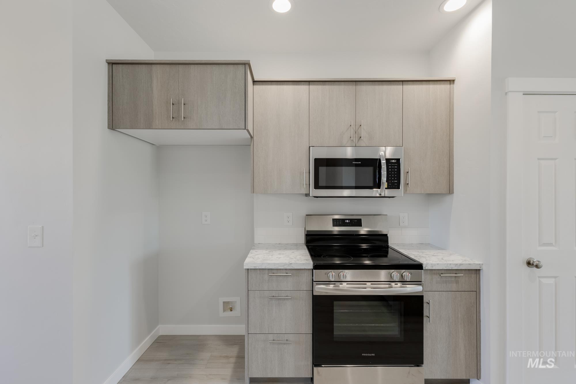 Kitchen with stainless steel appliances, light brown cabinetry, modern cabinets, light wood-style flooring, and light stone counters