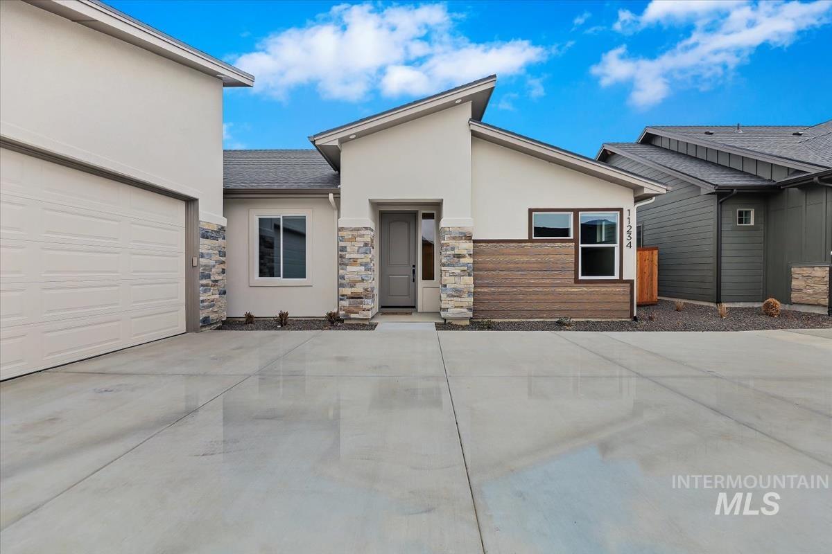 View of front of home with stucco siding, stone siding, a garage, and concrete driveway