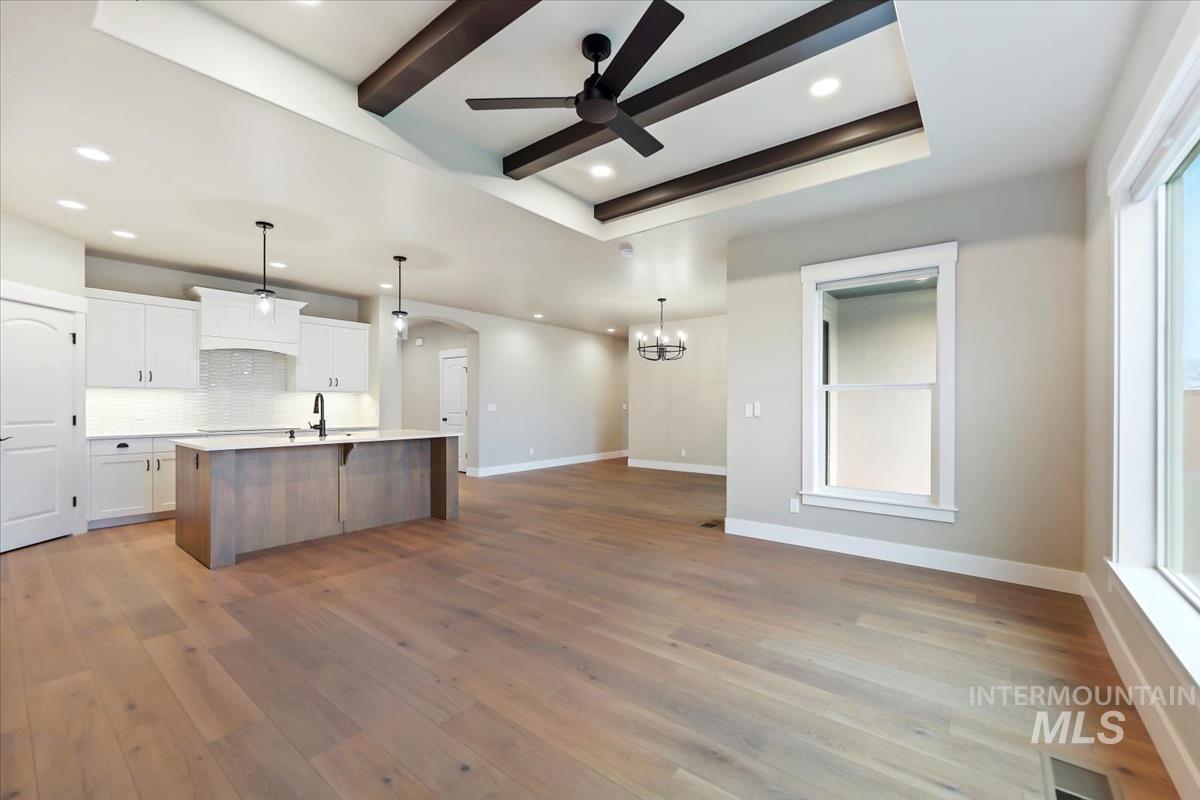 Kitchen with white cabinetry, arched walkways, open floor plan, hanging light fixtures, and beamed ceiling