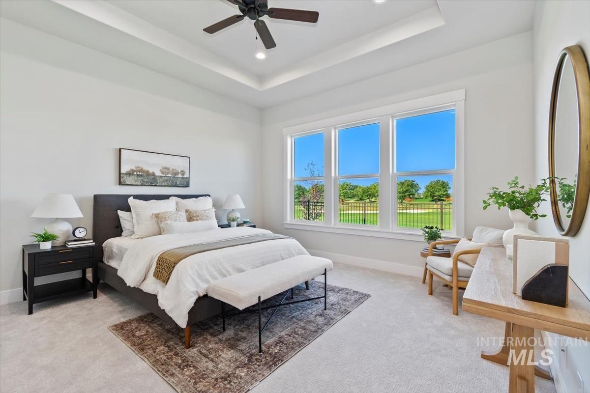 Bedroom with a raised ceiling, light colored carpet, ceiling fan, and recessed lighting