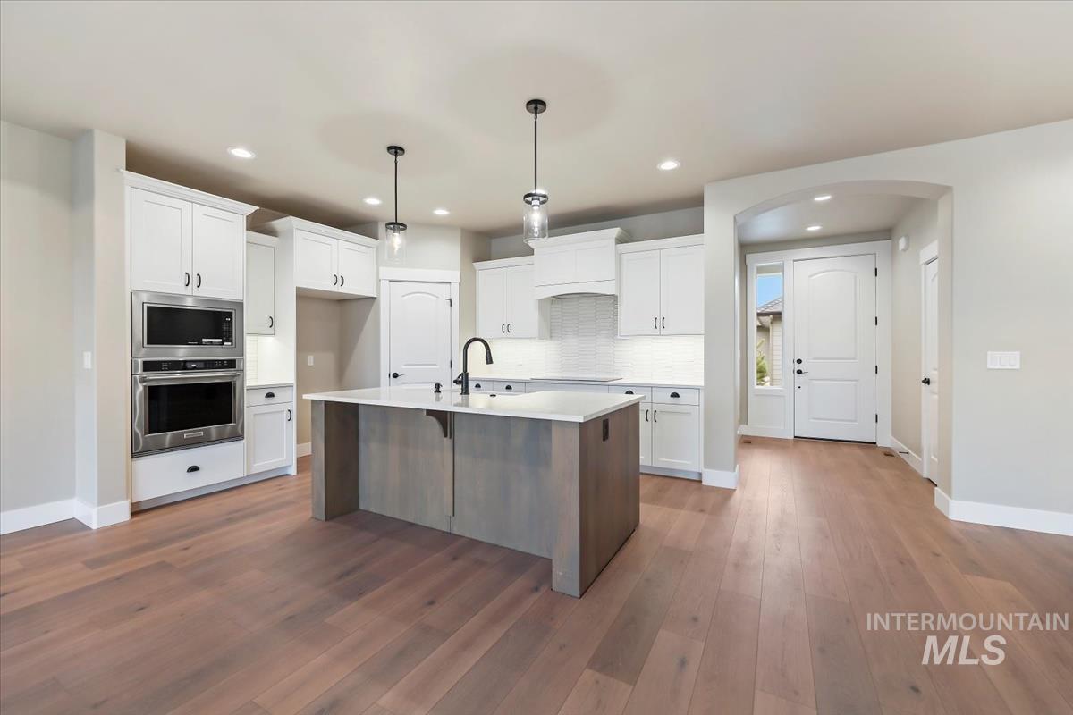Kitchen with a breakfast bar area, white cabinets, stainless steel appliances, a center island with sink, and pendant lighting