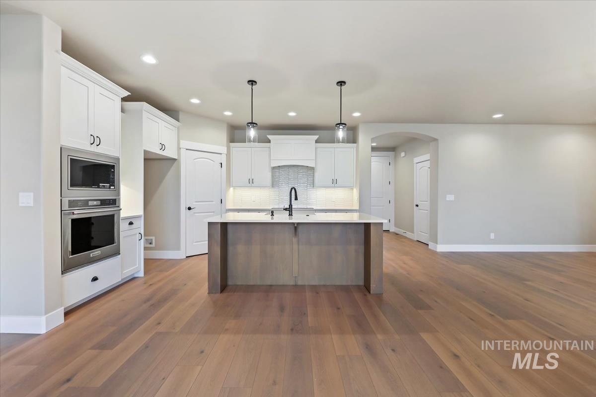 Kitchen featuring arched walkways, decorative light fixtures, appliances with stainless steel finishes, white cabinets, and recessed lighting