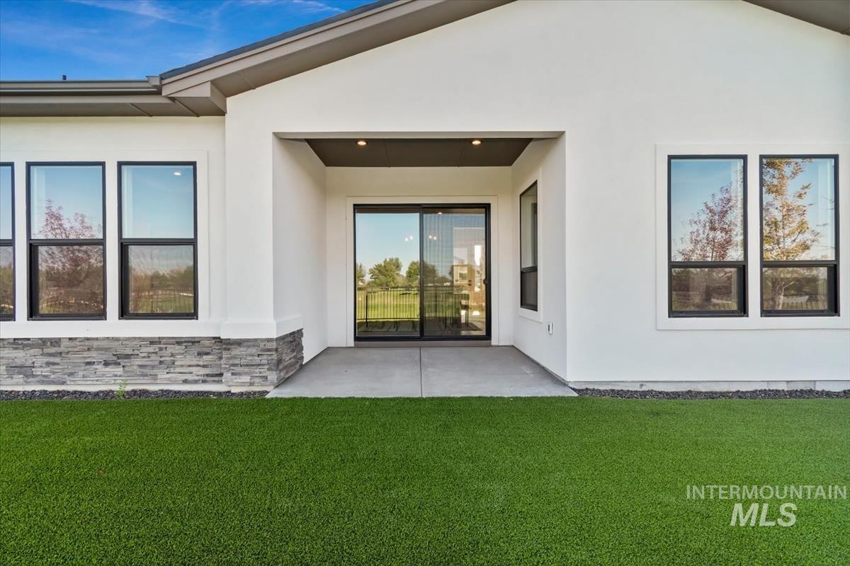 View of exterior entry featuring a patio, stucco siding, a lawn, and stone siding
