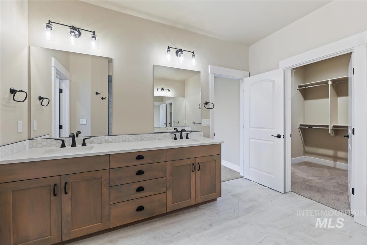 Bathroom with double vanity, a spacious closet, and light marble finish floors