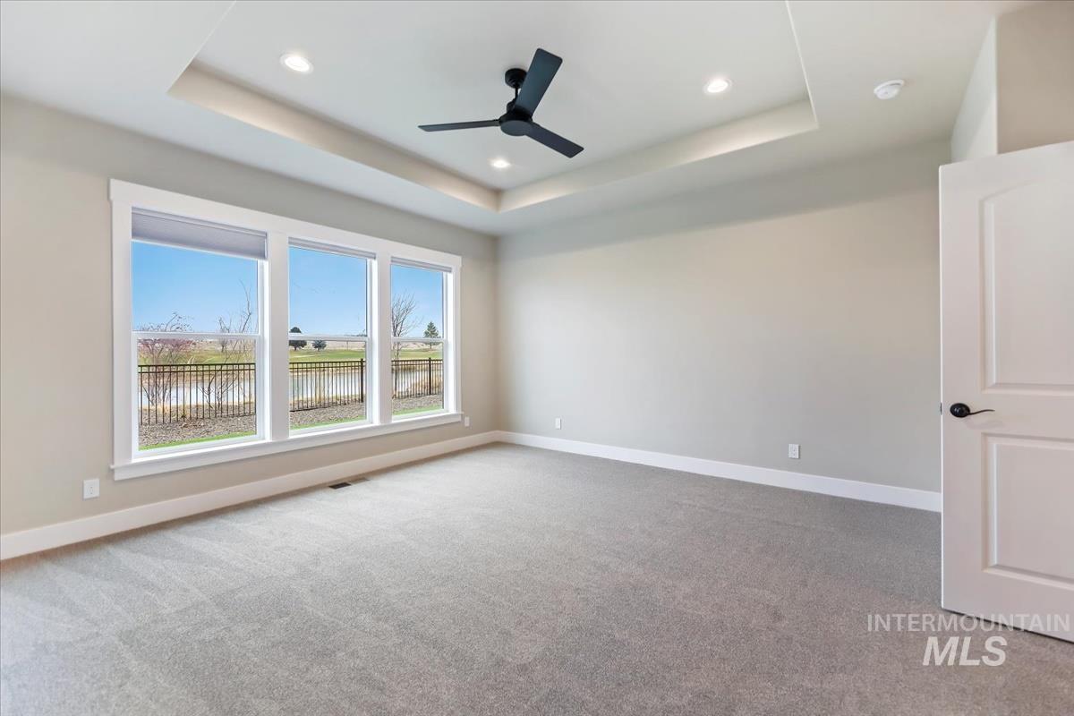 Spare room with light colored carpet, recessed lighting, a water view, a ceiling fan, and a tray ceiling