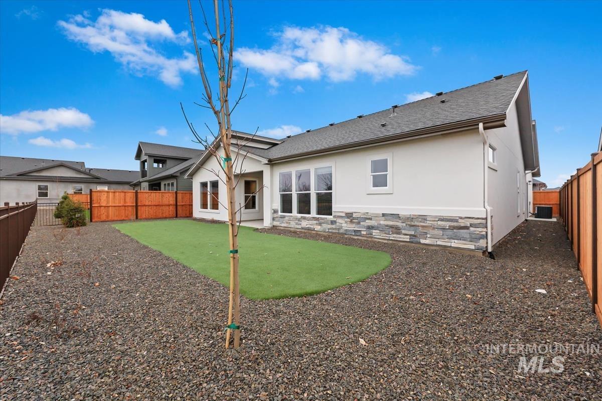 Rear view of house with stucco siding, stone siding, a fenced backyard, and a patio