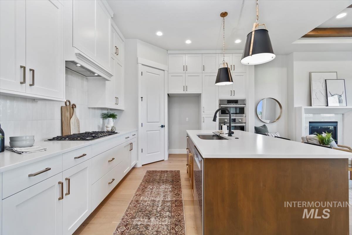 Kitchen featuring white cabinets, light wood-type flooring, an island with sink, pendant lighting, and recessed lighting