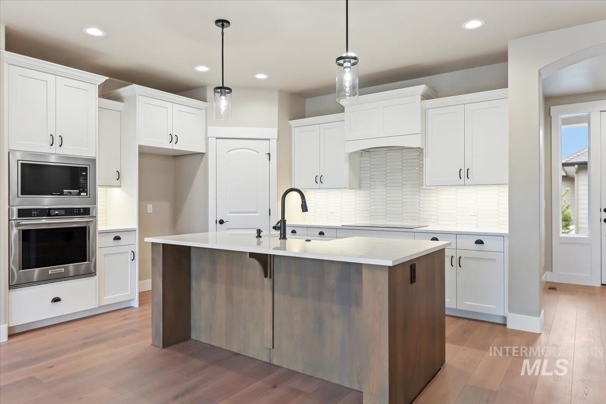 Kitchen featuring appliances with stainless steel finishes, white cabinetry, a center island with sink, light wood finished floors, and a breakfast bar area