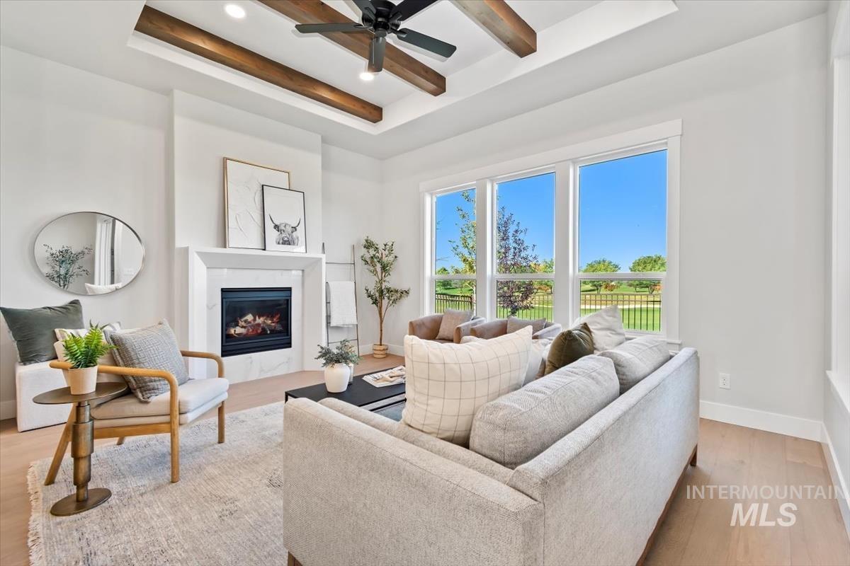 Living room featuring beamed ceiling, light wood-type flooring, a tray ceiling, a premium fireplace, and ceiling fan